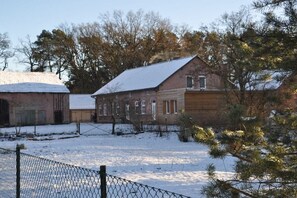 Un bâtiment en briques dont le toit est recouvert de neige, entouré d’arbres et d’une zone délimitée par une clôture.