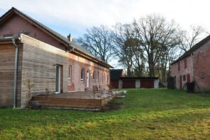 Een bakstenen gebouw met een houten uitbouw, een gazon en een boom op de achtergrond.