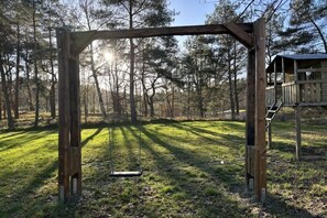 A wooden swing set in a wooded area with a wooden structure in the background. - Holiday home with 4 bedrooms (Gorlosen , OT Strassen)