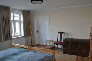 A room with a bed, a chair, a small table, a window with curtains, and a door. - Holiday home with 4 bedrooms (Gorlosen , OT Strassen)