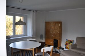Een kamer met een ronde tafel, stoelen, een bank, een kast en een raam met gordijnen.