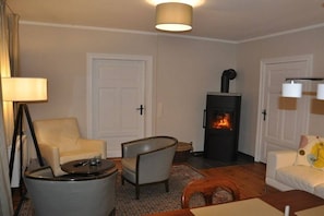 Un salon chaleureux avec une cheminée, deux fauteuils, une petite table et une lampe.
