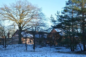 A snow-covered landscape with a large tree and a building with a conical roof. - Holiday home with 4 bedrooms (Gorlosen , OT Strassen)