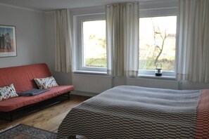 Een kamer met een bed, een slaapbank, een raam met gordijnen en een radiator.