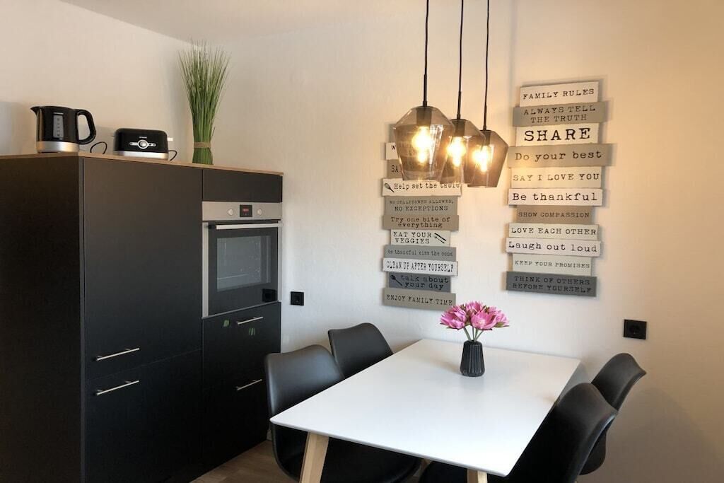 A modern kitchen with a dining area, featuring a white table, black chairs, and a wall with inspirational quotes.