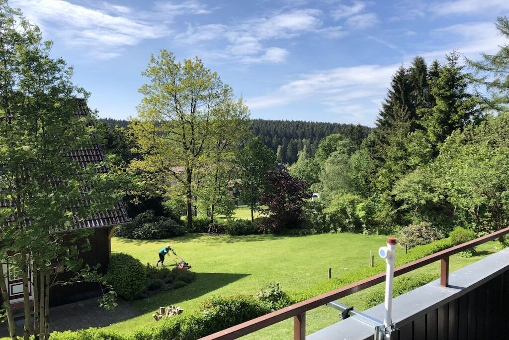 A residential property with a well-maintained lawn, a wooden deck, and a view of a forested area.