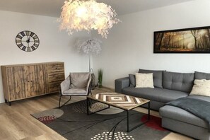 A modern living room with a grey sofa, a wooden cabinet, a round clock, and a large abstract painting. - Holiday apartment with 1 bedroom (Hahnenklee Bockswiese)