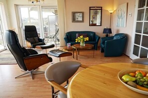 A living room with a wooden dining table, two sofas, a black leather chair, and a coffee table with a vase of flowers. - Residence Juliana 47 (Julianadorp)