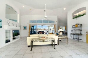 A spacious living room with a high ceiling, a white sofa, a glass coffee table, and a television. - CCVS - Dream Villa Mango Bay (Cape Coral)