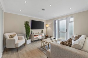 A modern living room with a sofa, armchair, coffee table, and a TV mounted on the wall. - New! Stylish 1BR Flat in Lewisham (Greater London)