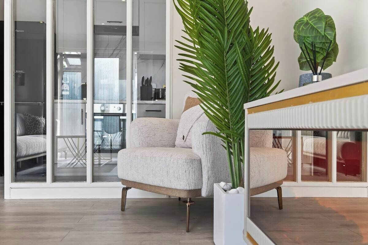 Ein modernes Wohnzimmer mit einer Couch, einer großen Zimmerpflanze und Blick durch Glastüren auf einen Essbereich.