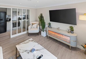 A modern living room with a marble coffee table, a flat-screen TV, a sofa, and a kitchen in the background. - New! Stylish 1BR Flat in Lewisham (Greater London)