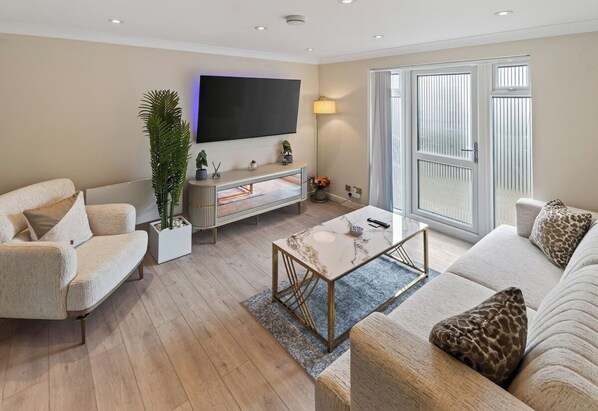 A modern living room with a flat-screen TV, a sofa, a coffee table, and a plant. - New! Stylish 1BR Flat in Lewisham (Greater London)