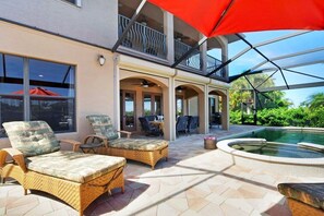Un espace extérieur abrité, aménagé avec des meubles en osier, une piscine et un balcon fermé par des baies vitrées.