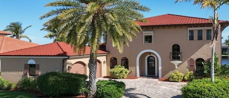 A two-story building with a red-tiled roof, arched windows, and a paved entrance.