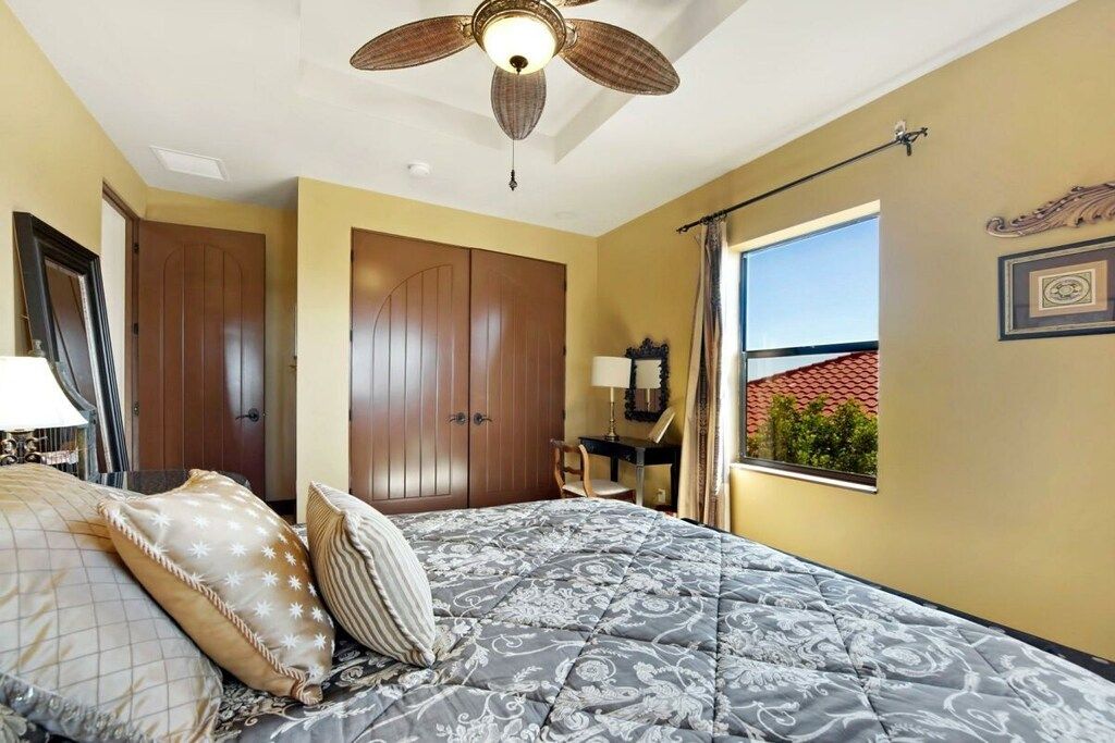 A bedroom with a bed, a ceiling fan, a window with a view, and a door.