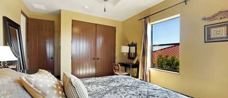 A bedroom with a bed, a ceiling fan, a window with a view, and a door.