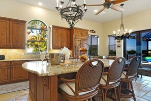 A kitchen with wooden cabinets, a granite countertop, and a dining area with wicker chairs. - CCVS - Villa Kara Tuscany (Cape Coral, FL)