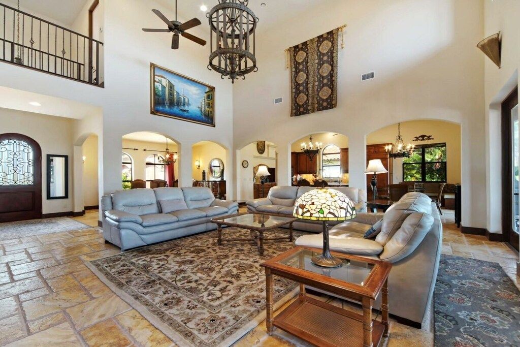 A spacious living room with a high ceiling, a chandelier, and a large painting.