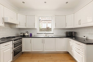 A modern kitchen with white cabinets, a black countertop, and stainless steel appliances. - New! Charming 1BR Maisonette | Alexandra Park (Greater London)