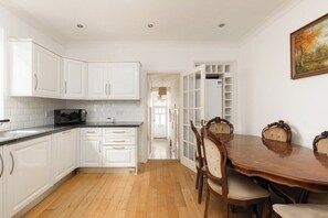 A kitchen with white cabinets, a wooden dining table with chairs, and a view into the dining area. - New! Charming 1BR Maisonette | Alexandra Park (Greater London)