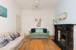 A living room with a sofa, a fireplace, and a chandelier. - New! Charming 1BR Maisonette | Alexandra Park (Greater London)