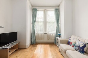 A living room with a television, sofa, and windows with curtains. - New! Charming 1BR Maisonette | Alexandra Park (Greater London)
