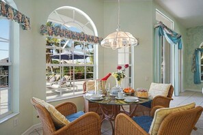 A dining area with wicker chairs, a round table, and a hanging light fixture. - CCVS - Villa White Diamond (Cape Coral)
