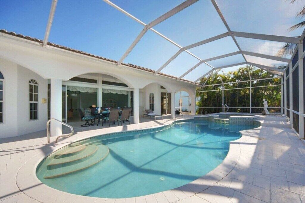 Ein Schwimmbecken mit Glasüberdachung, umgeben von einer Terrasse mit Gartenmöbeln.