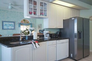 A kitchen with white cabinets, a stainless steel refrigerator, a coffee maker, and a window with curtains. - CCVS - Villa White Diamond (Cape Coral)