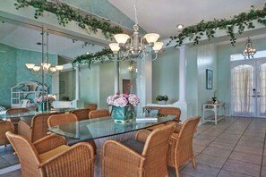 A dining area with a glass table surrounded by wicker chairs, a chandelier, and a vase with flowers. - CCVS - Villa White Diamond (Cape Coral)