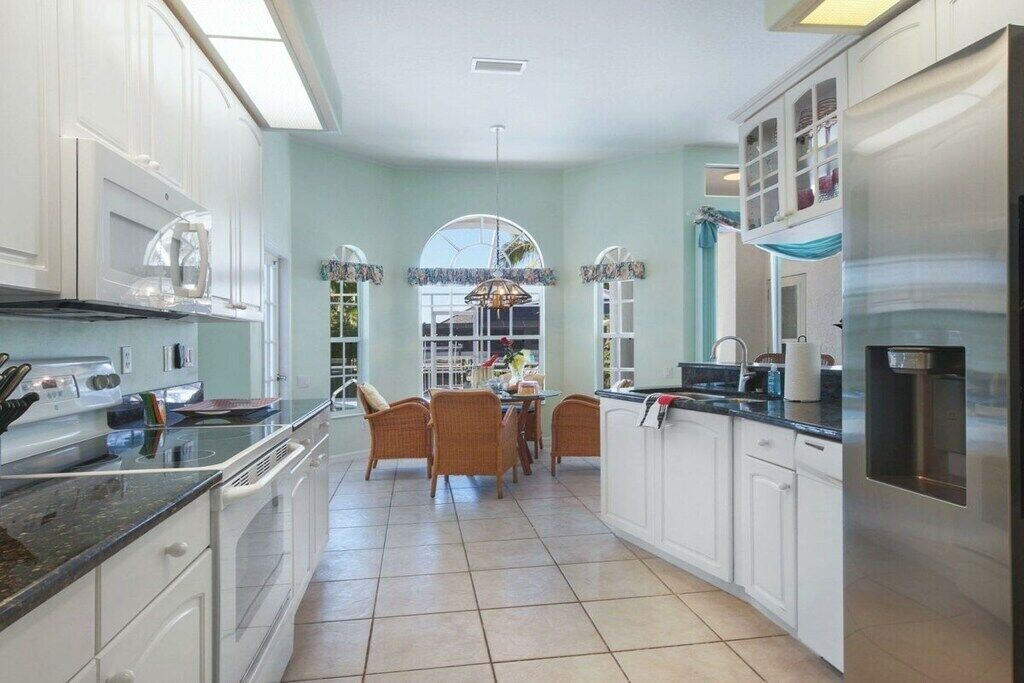 A kitchen with white cabinets, a stainless steel refrigerator, and a dining area with wicker chairs.