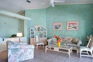 A living room with a teal wall, a sofa, a coffee table, and two chairs. There are two framed pictures on the wall. - CCVS - Villa White Diamond (Cape Coral)