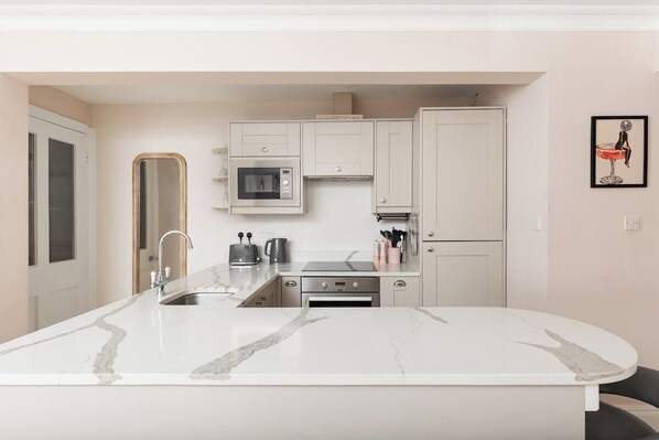 A modern kitchen with a marble countertop, built-in appliances, and a minimalist design. - New! West Kensington 2BR Gem w/Garden & Patio (Greater London)