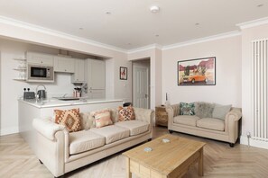 A living room with a sofa, a coffee table, and a kitchen area with a microwave and cabinets. - New! West Kensington 2BR Gem w/Garden & Patio (Greater London)