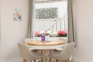 A dining area with a round table, two chairs, a window with curtains, and a framed picture on the wall. - New! West Kensington 2BR Gem w/Garden & Patio (Greater London)