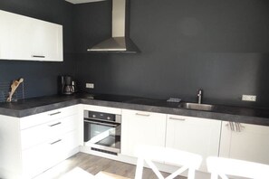 A modern kitchen with white cabinets, a black countertop, and a stainless steel sink. - Holiday apartment for 2-4 people (oostkapelle)