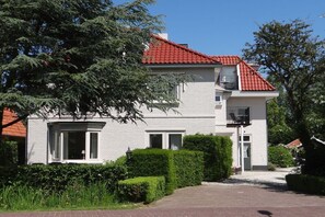 A two-story house with a red-tiled roof, white exterior walls, and a front entrance with a small porch. - Holiday apartment for 2-4 people (oostkapelle)