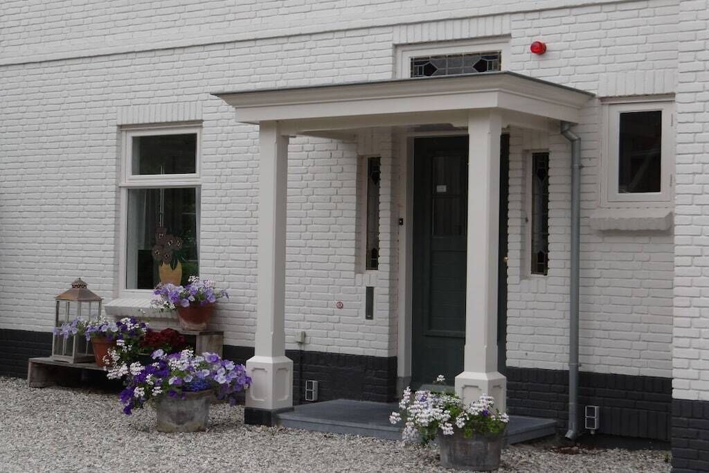 A white building with a black-framed entrance, a small porch, and flower pots on the ground.
