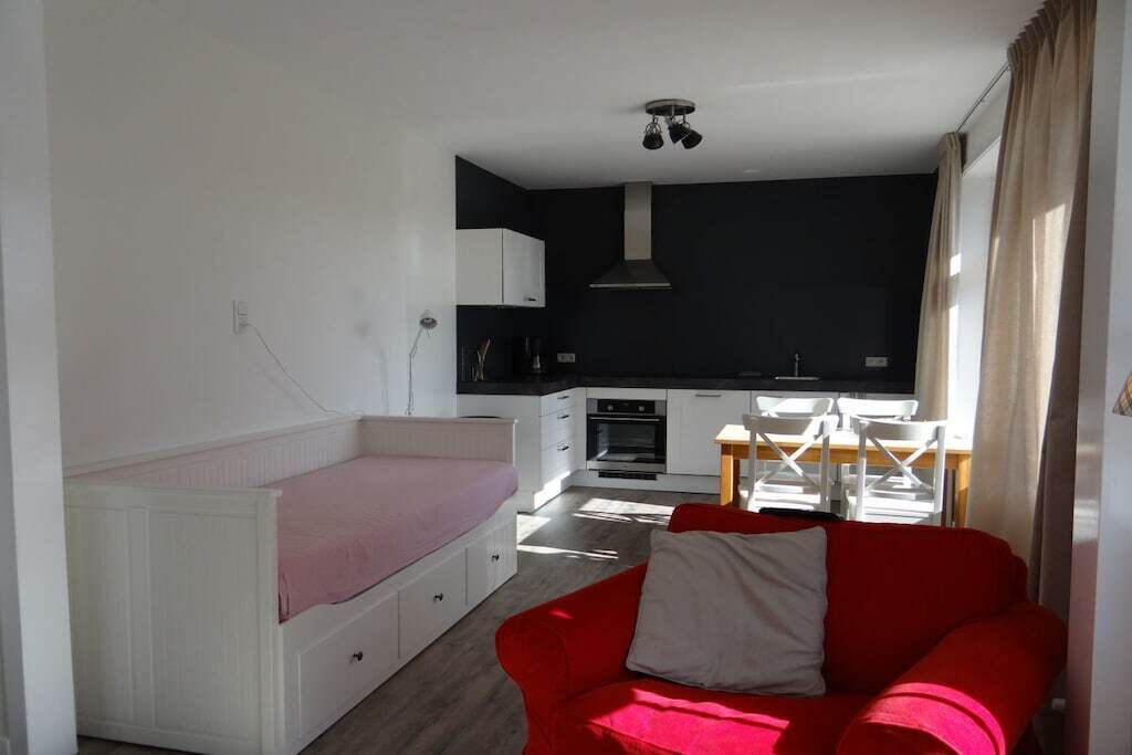 Kompakti oleskelutila, jossa on pieni keittiönurkkaus, ruokailualue ja punainen sohva.