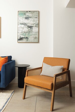 Ein Zimmer mit einem blauen Sofa, einem braunen Ledersessel, einem runden schwarzen Tisch und einem Gemälde an der Wand.