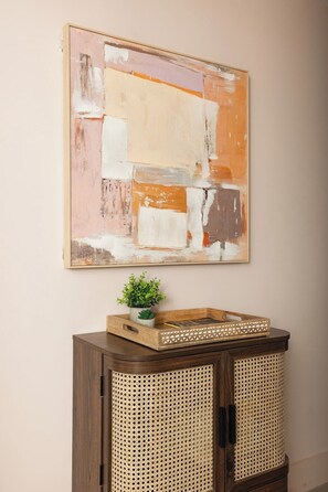 A wall-mounted abstract painting with a wooden cabinet below featuring a woven basket and a potted plant. - New! Stylish 1BR Flat w/Patio in Vibrant Peckham (Greater London)