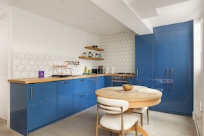 Een moderne keuken met blauwe kastjes, een houten aanrecht en een ronde eettafel met stoelen.