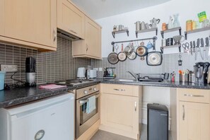 A kitchen with a built-in oven, a dishwasher, and a sink. There are hanging pots and pans on the wall, and a coffee maker on the counter. - New! Canal-side 1BR Flat in Clapton (Greater London)