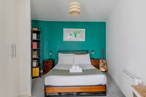 A neatly made bed with a green blanket, a wall map, and a guitar on the nightstand. - New! Canal-side 1BR Flat in Clapton (Greater London)