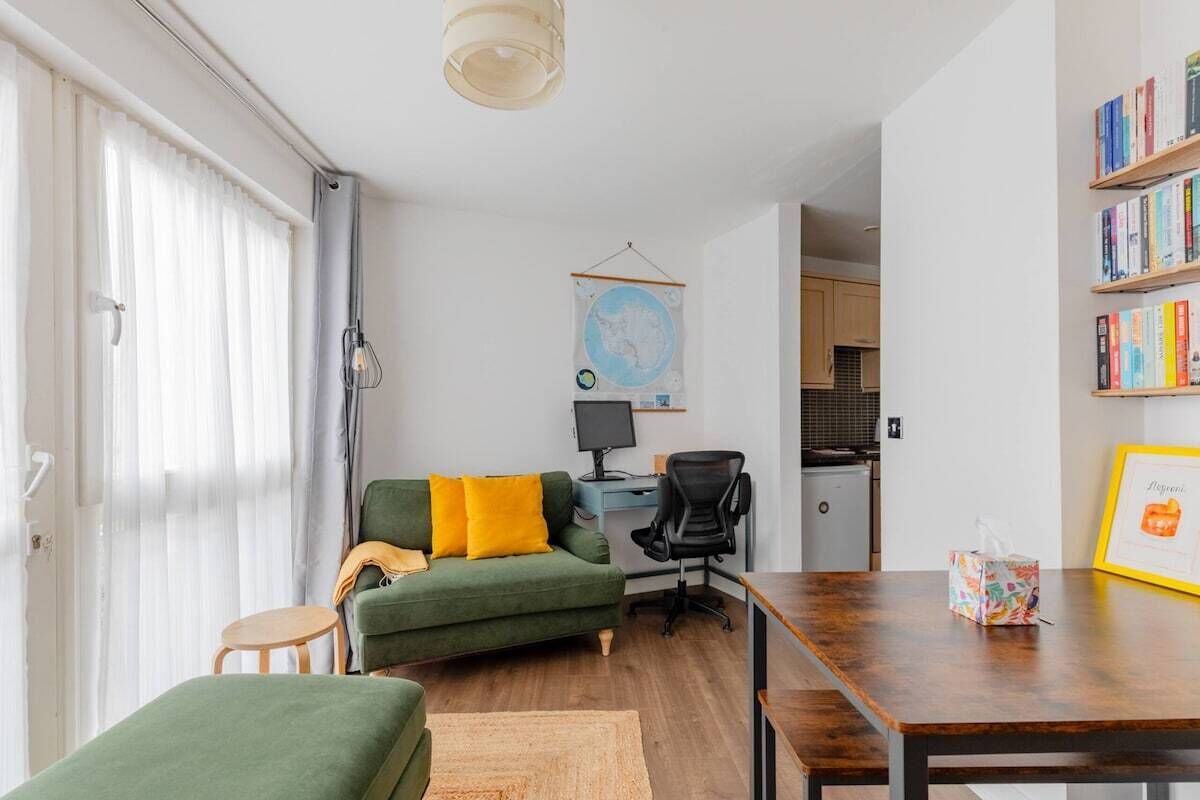 Een moderne woonkamer met een groene bank, een houten eettafel en een keuken op de achtergrond.