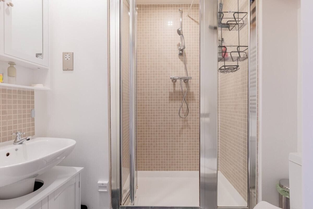 Ein Badezimmer mit einem weißen Waschbecken, einer Duschkabine aus Glas und einer gefliesten Wand.