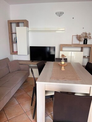 Un soggiorno moderno con divano, tavolo da pranzo, sedie, televisore a schermo piatto e scaffalature integrate.