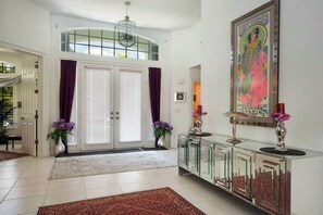 Un hall d’entrée spacieux, doté d’une double porte à vitrine, d’une console décorative et d’une œuvre d’art encadrée accrochée au mur.