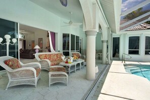 Ein überdachter Außenbereich mit Korbmöbeln, einem Pool und Blick ins Innere.